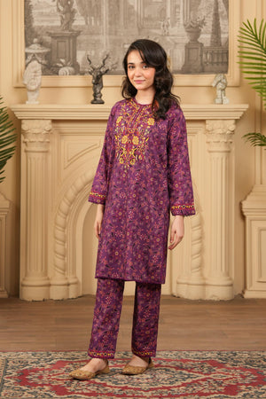Woman wearing a purple embroidered outfit standing in a decorated room with a fireplace.