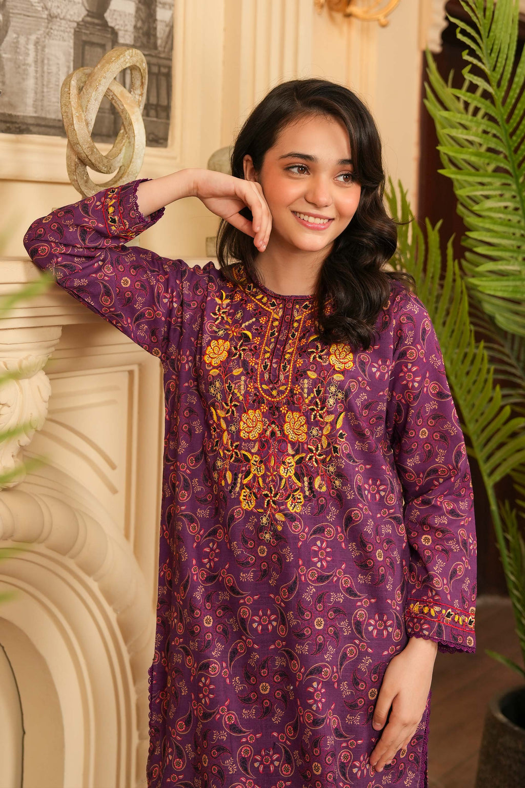 Woman wearing a purple embroidered kurta in an indoor setting with decorative elements.
