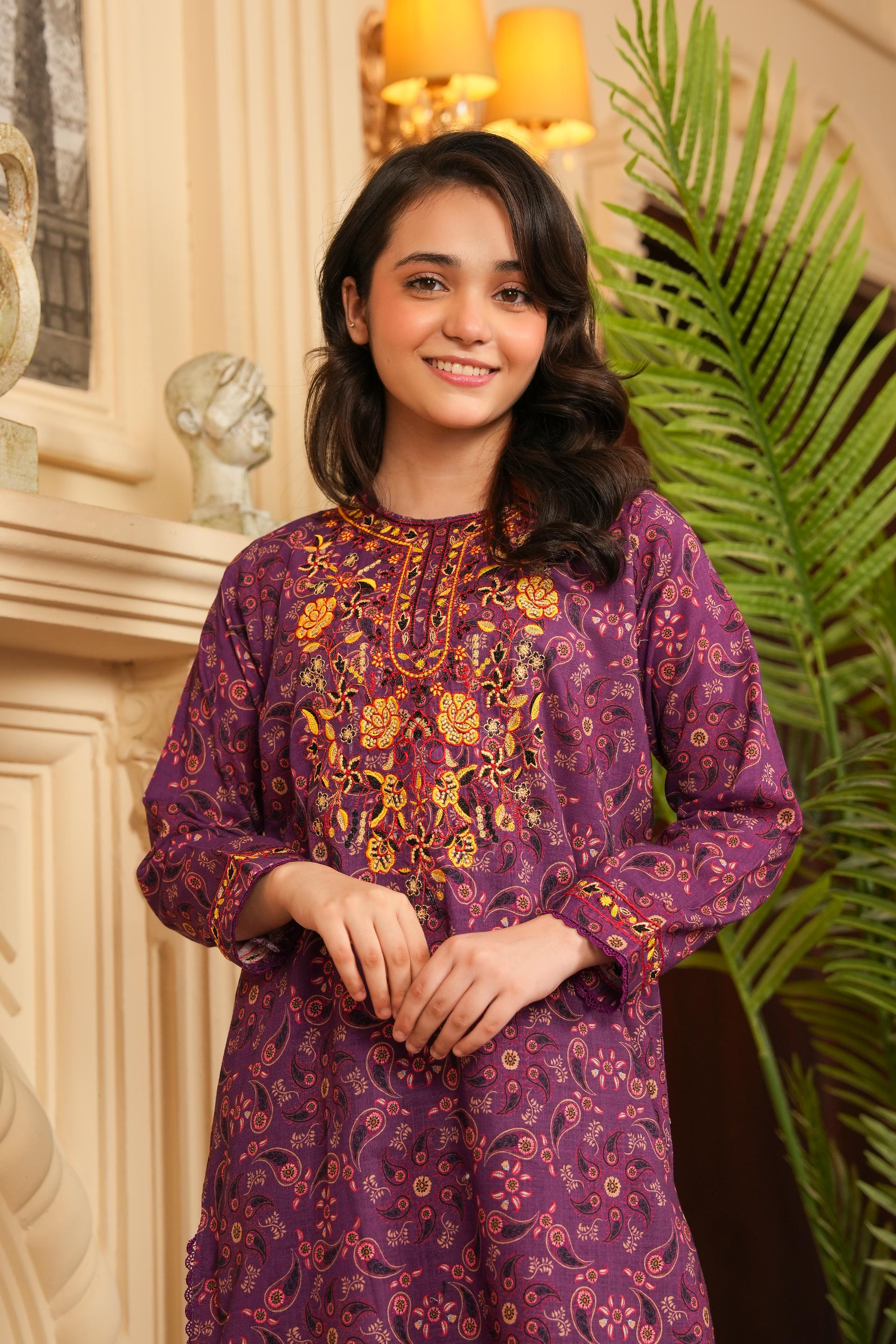 Woman wearing a purple floral patterned dress standing indoors with decorative elements.