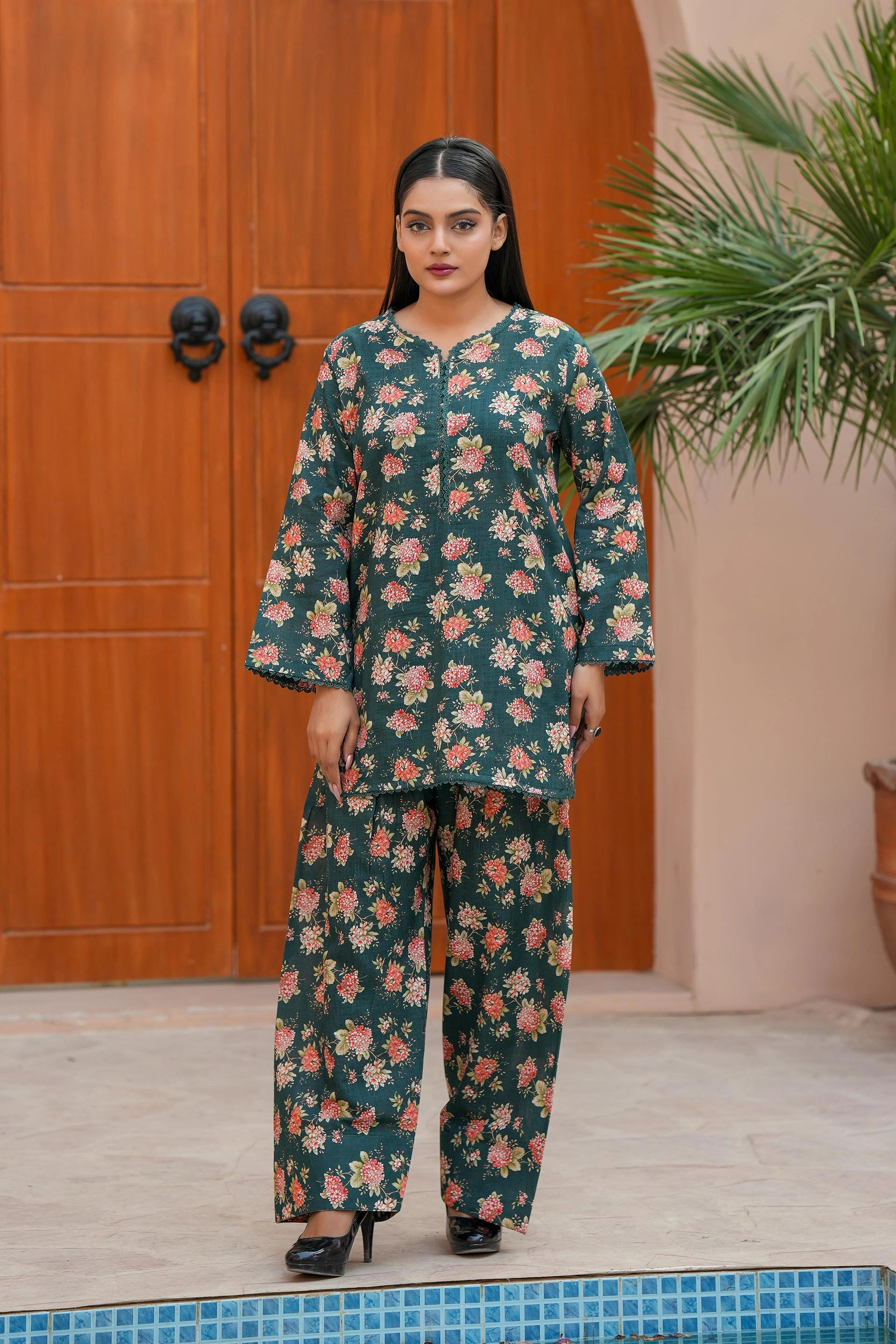 Woman wearing a floral outfit standing in front of a wooden door.