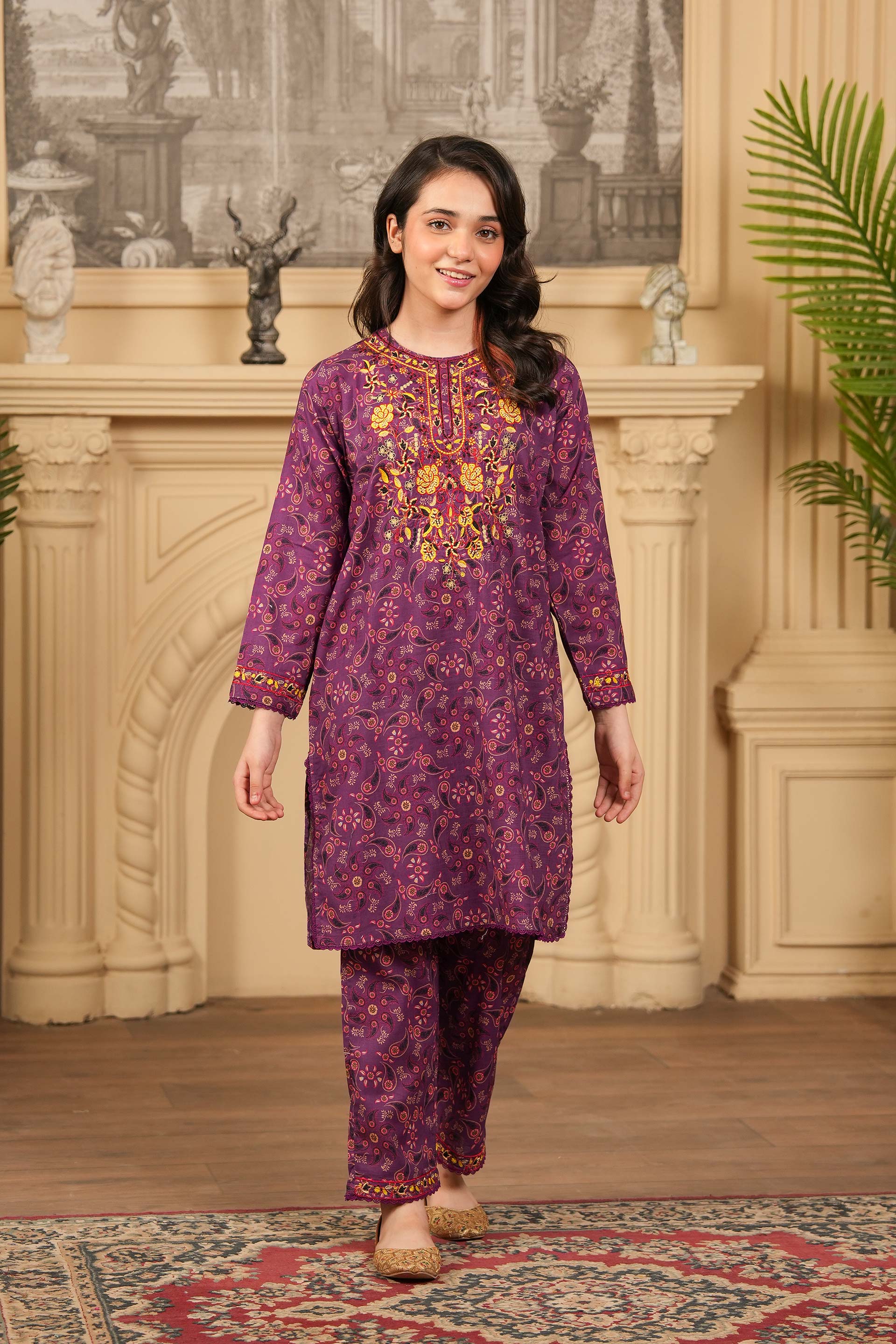 Woman wearing a purple embroidered traditional outfit in a decorated room.
