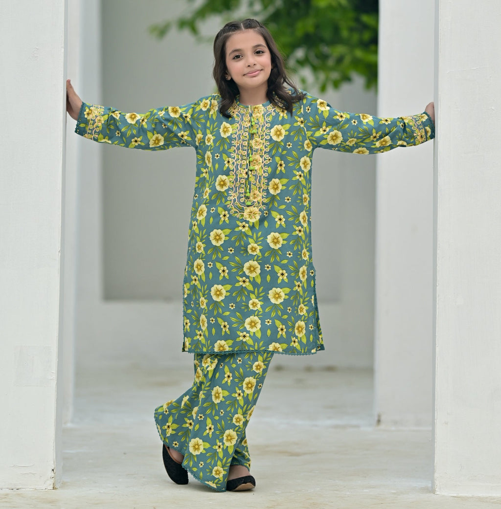 Woman in a green floral outfit standing in front of a white archway with greenery outside.