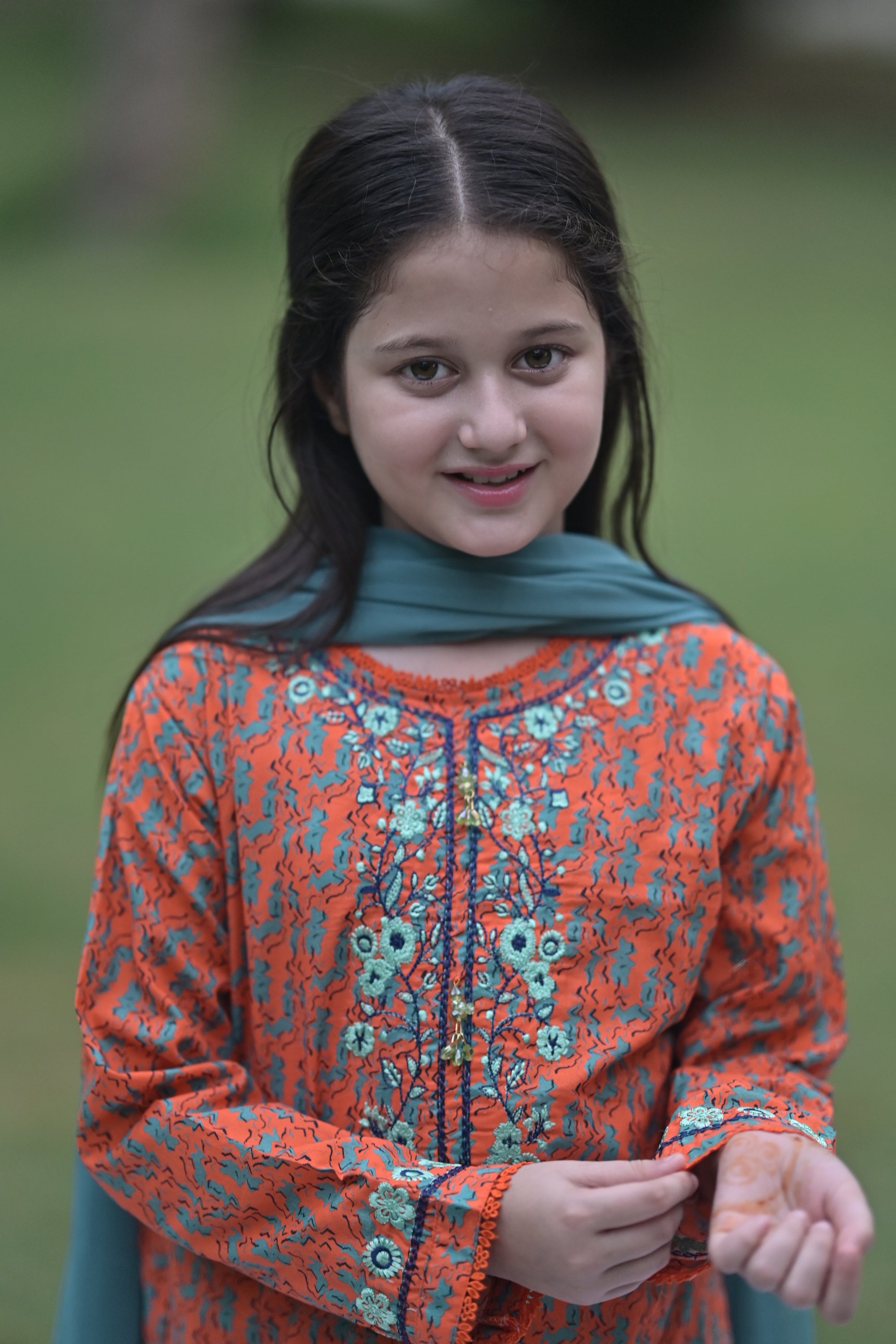 Girl wearing Nims Apparel orange floral embroidered traditional dress with teal scarf outdoors